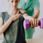 Mujer realizando ejercicios de rehabilitación con una pesa morada, asistida por un fisioterapeuta en un entorno clínico.