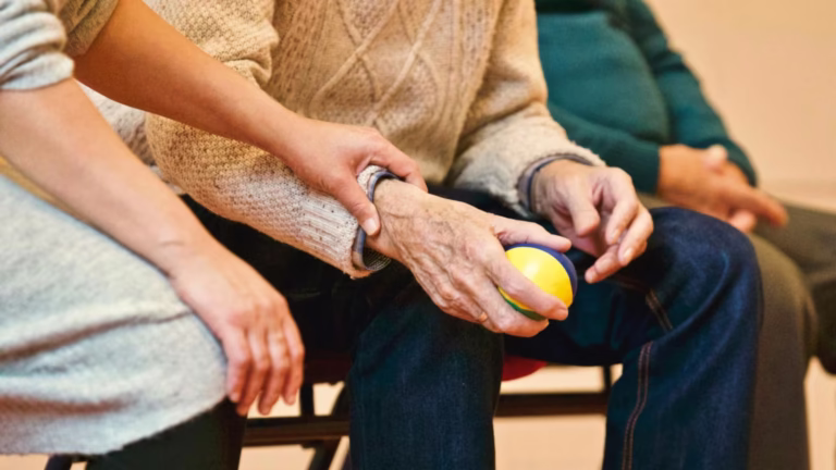 Persona mayor realizando ejercicios de rehabilitación con una pelota terapéutica, asistida por un fisioterapeuta. La imagen ilustra la importancia de la rehabilitación en el tratamiento ortopédico.