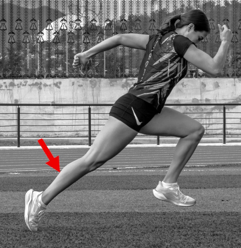 Corredora con flecha señalando la pierna posterior para explicar una posible lesión muscular durante la carrera.